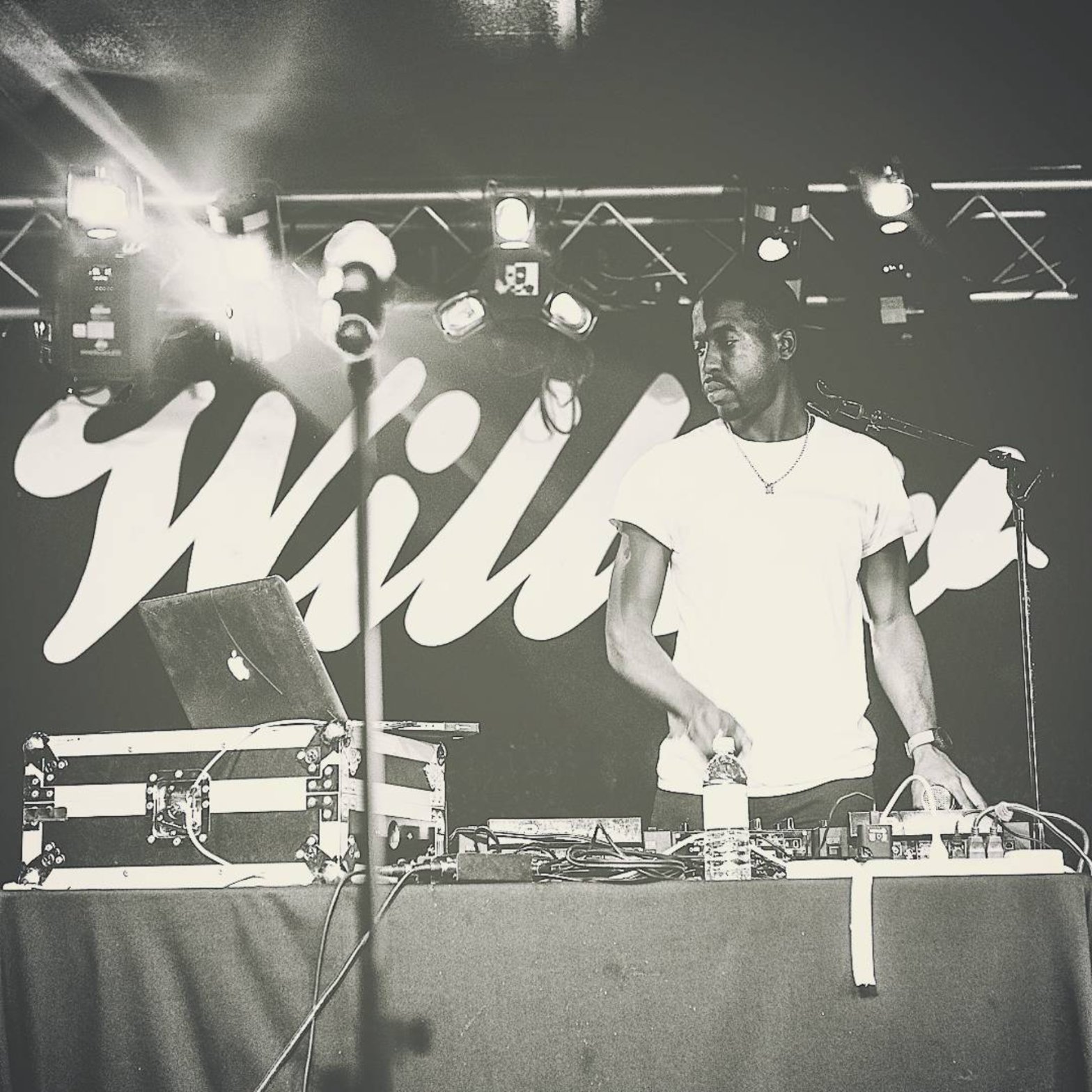 Black and white photo of DJ Roco behind two turntables under stage lights